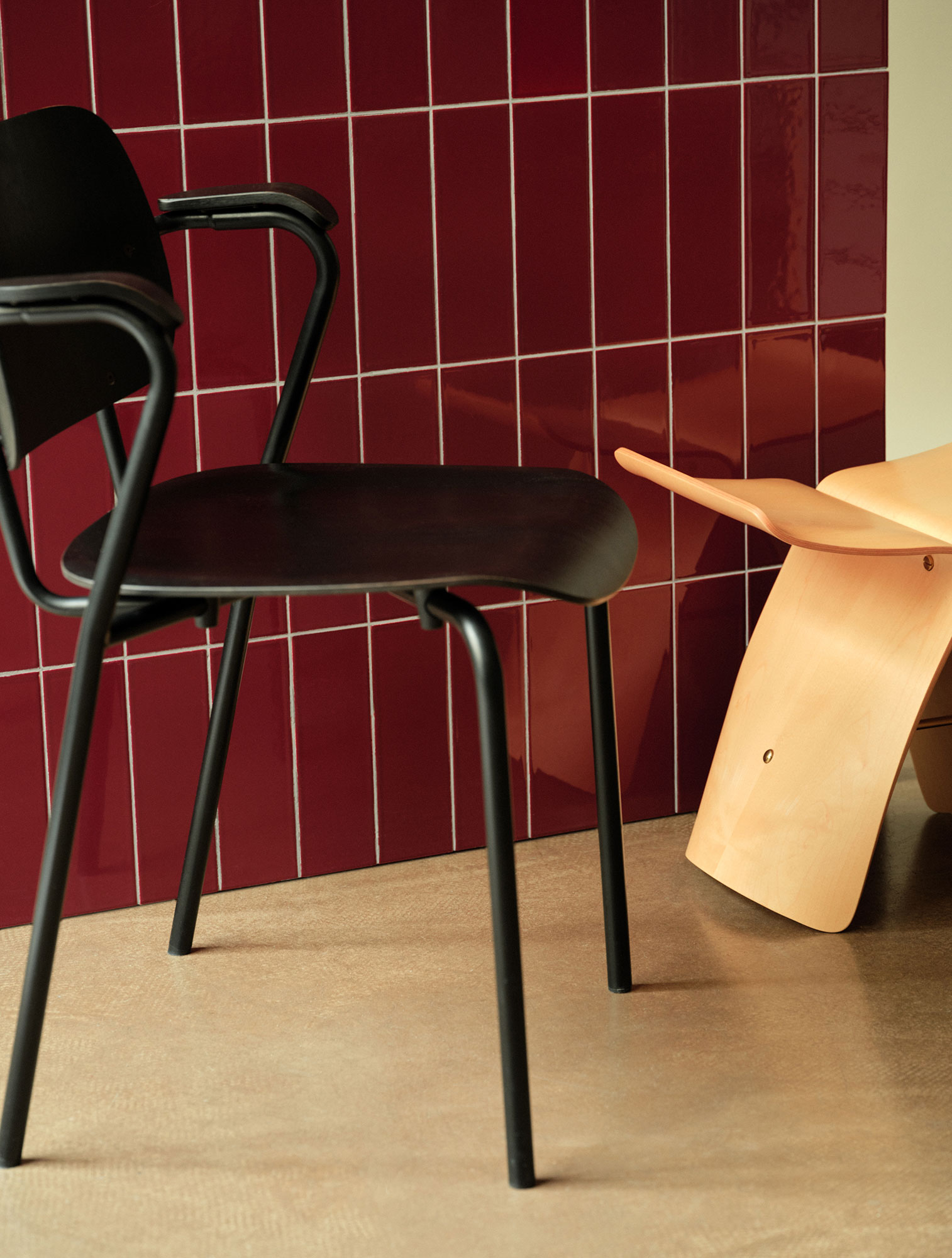 A black chair and a butterfly stool in front of a rosewood tilled wall.